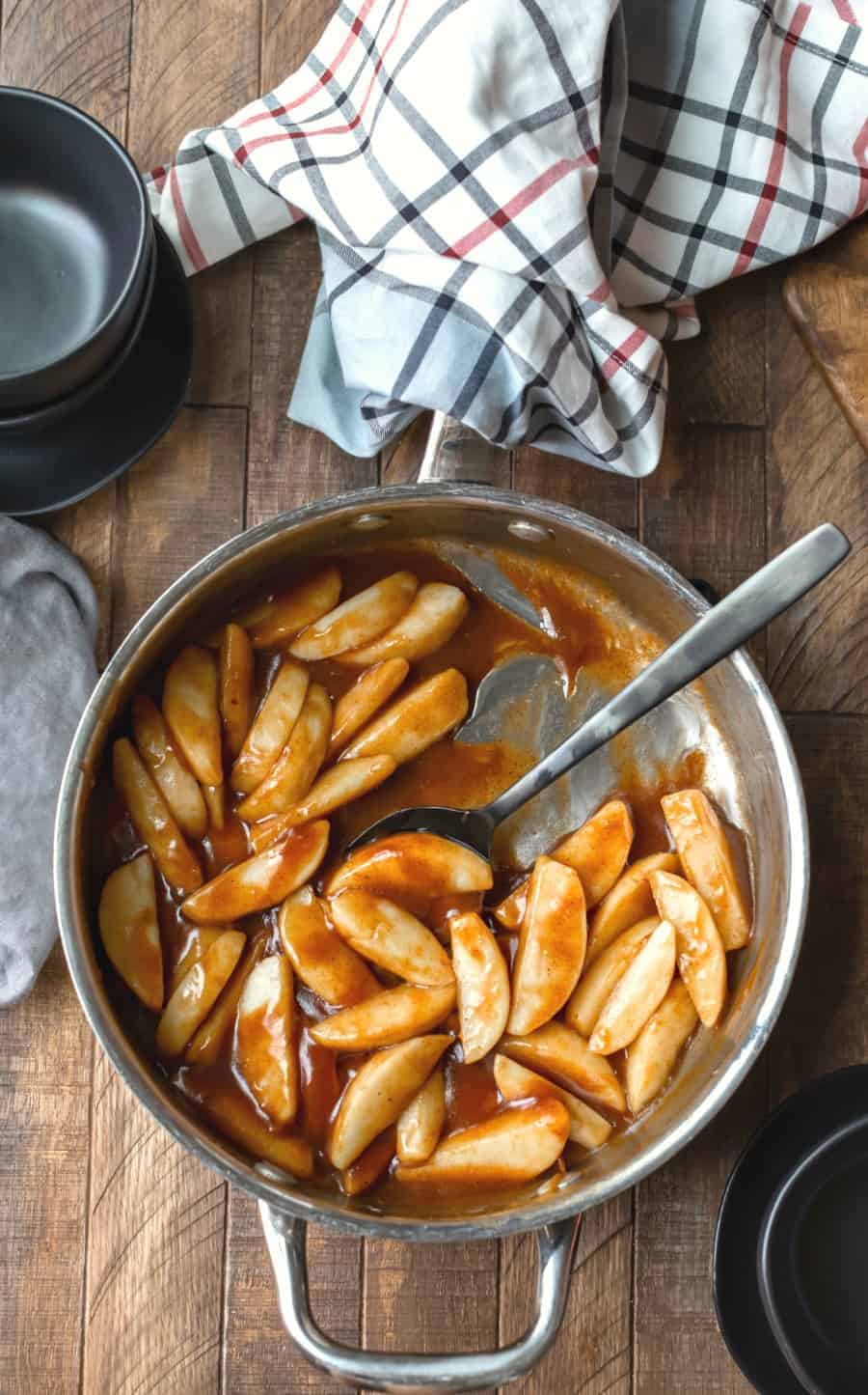 Cinnamon Apples in a silver skillet with a black spoon scooping up apples