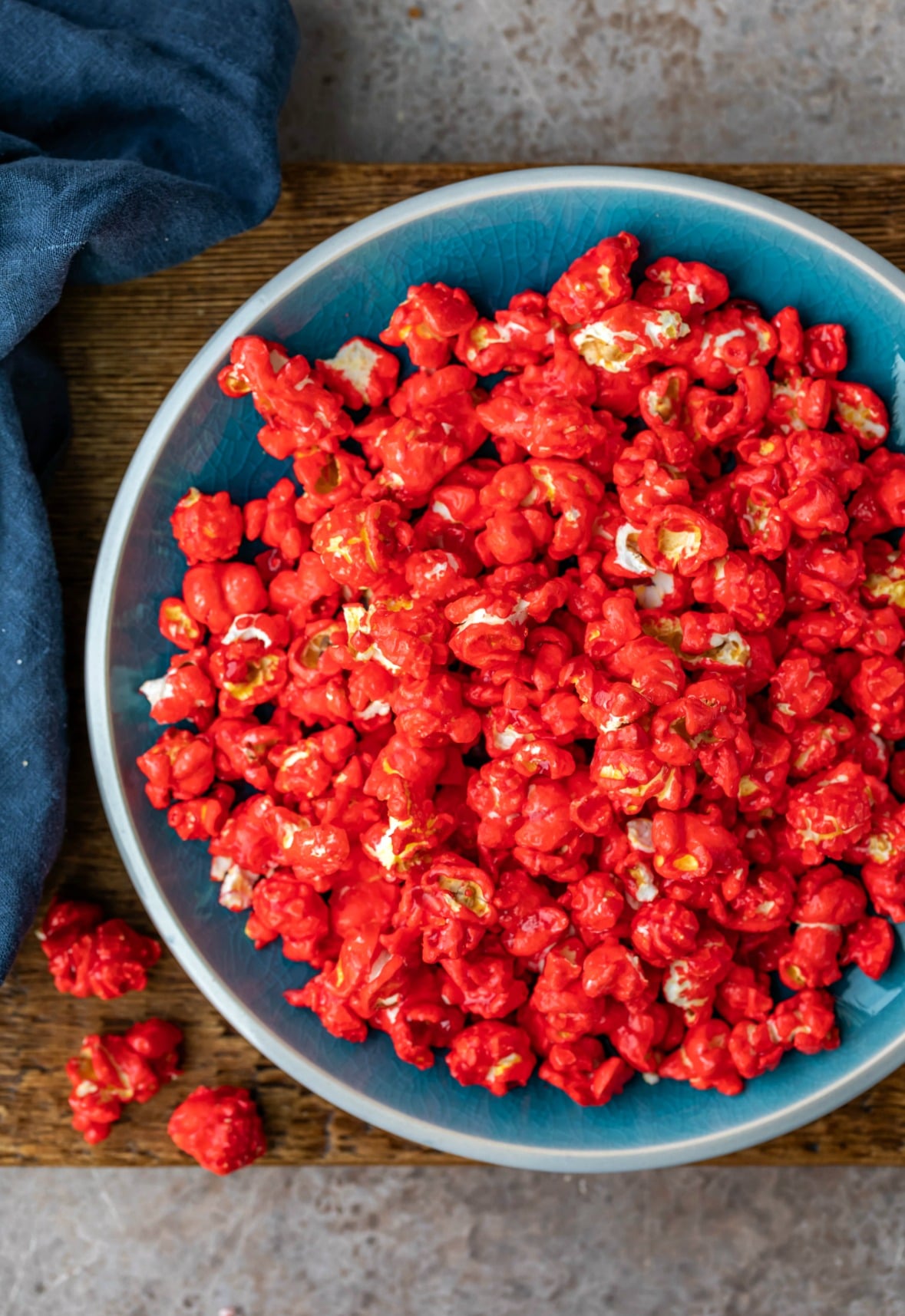 Plate of red hot cinnamon popcorn next to a blue linen napkin