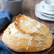 No Knead Bread on a wooden cutting board next to a blue napkin