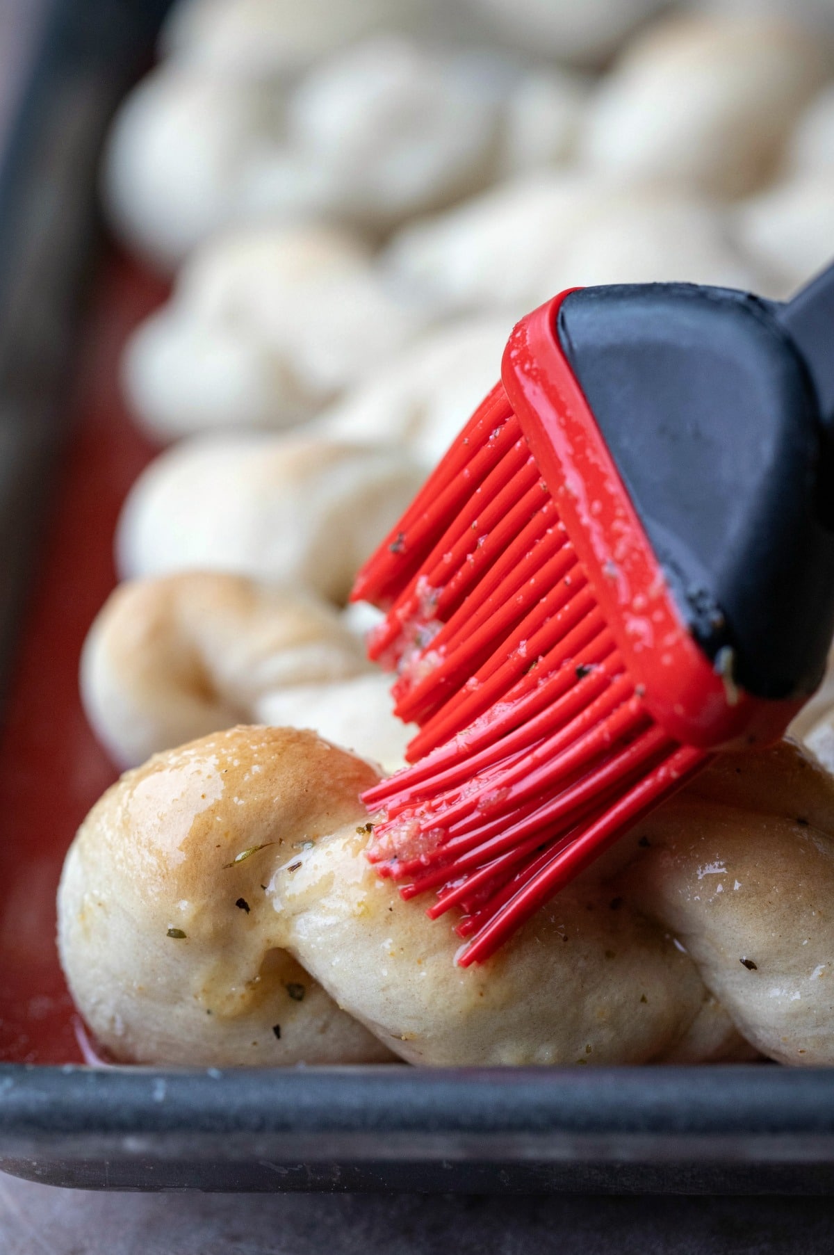 Silicone basting brush spreading garlic butter onto homemade breadsticks