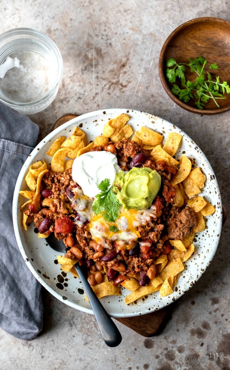 Plate of frito chili pie topped with sour cream and guacamole
