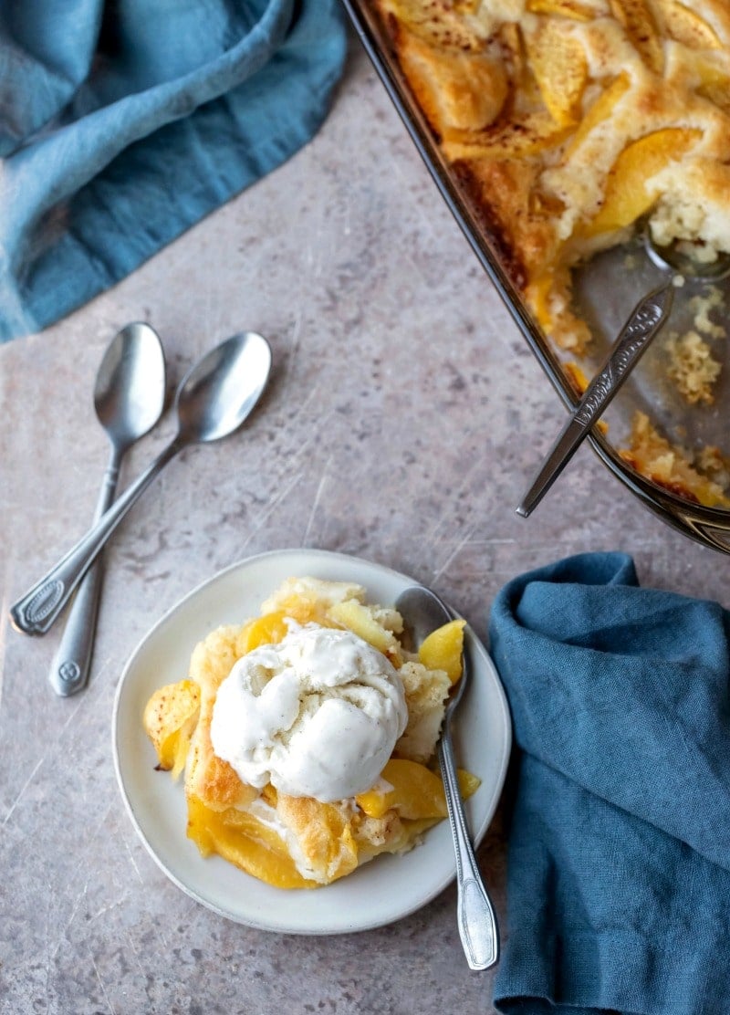 Dish of peach cobbler topped with a scoop of vanilla ice cream