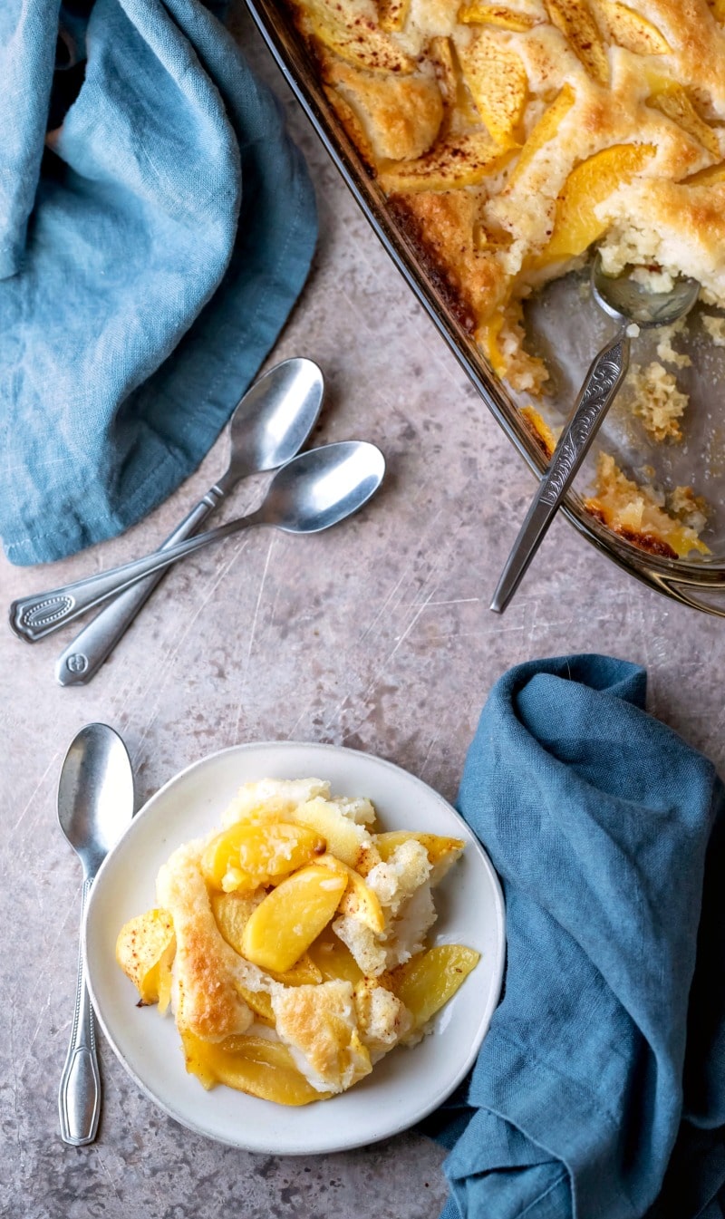 Dish of peach cobbler next to a silver spoon and blue linen napkin