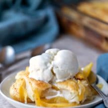 Dish of peach cobbler topped with a scoop of vanilla bean ice cream