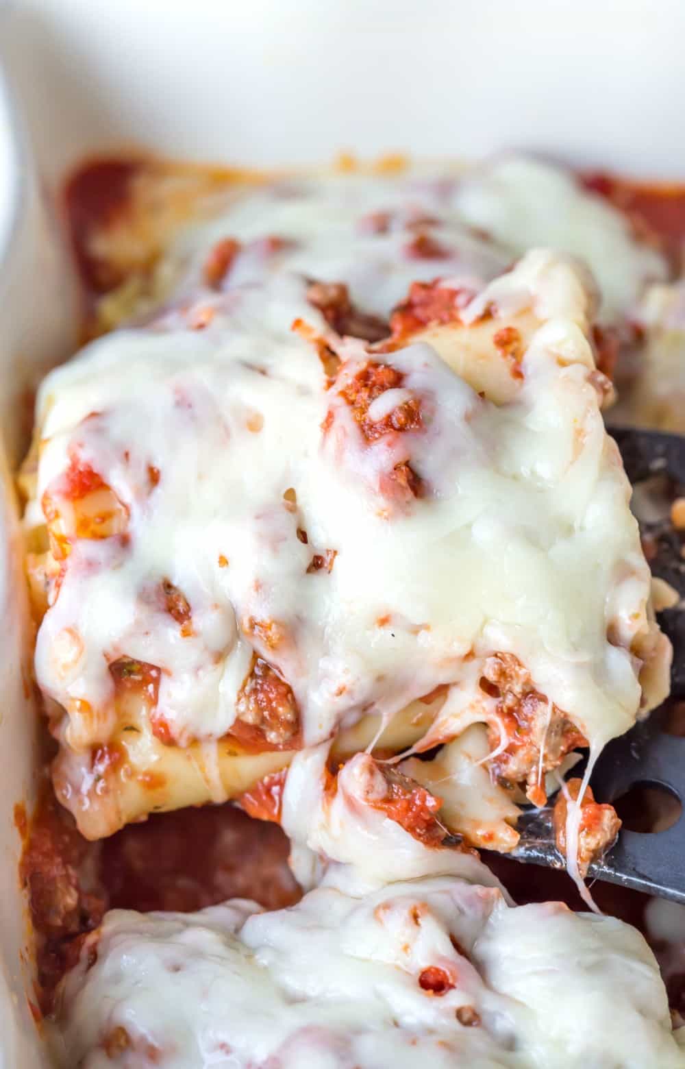 Lasagna Roll-Up on a spatula in a white baking dish