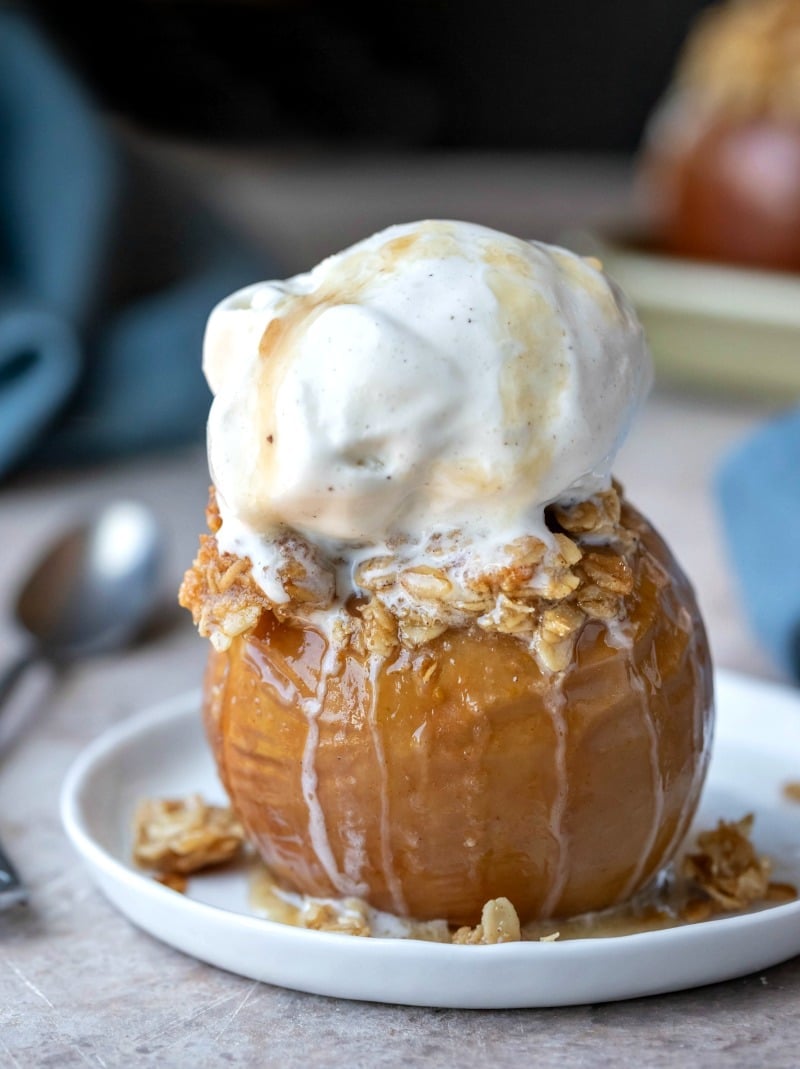 Baked apple on a white rimmed plate next to a silver spoon