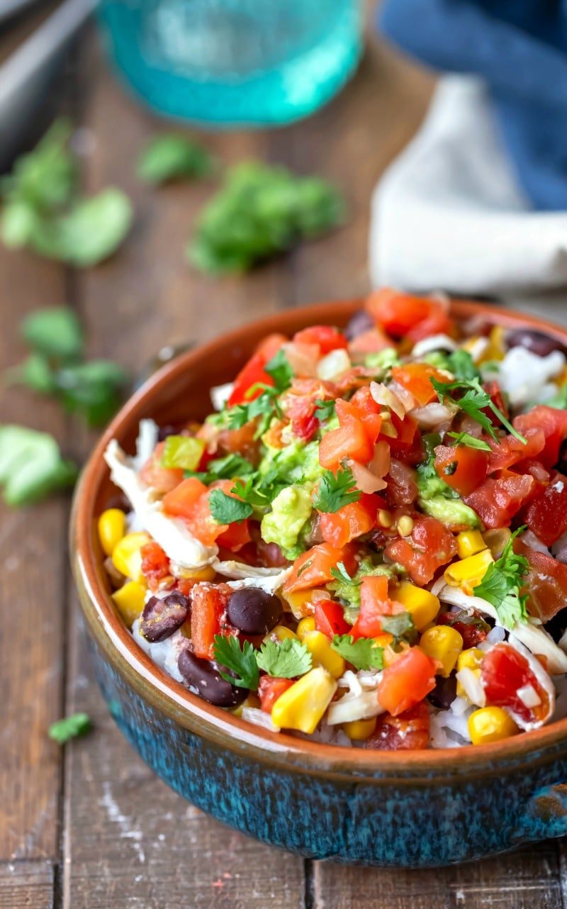 Crock pot Mexican chicken in a blue bowl topped next to a blue glass