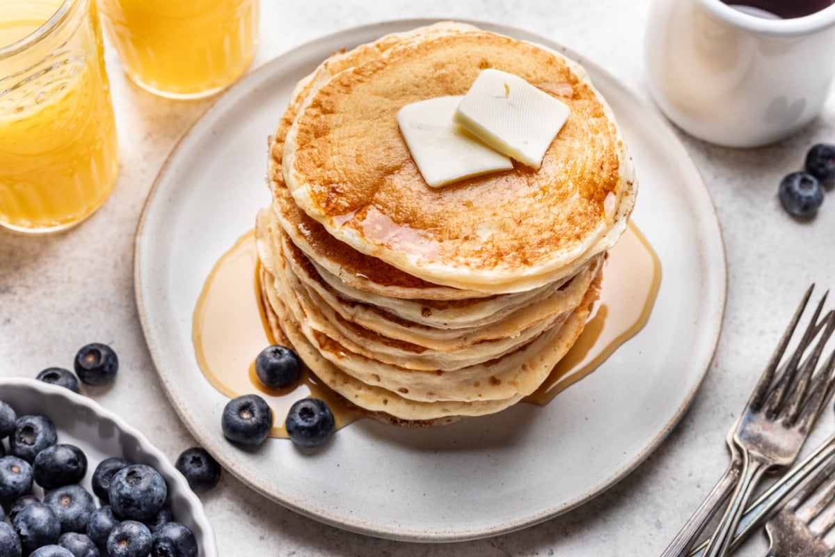 A stack of homemade buttermilk pancakes next to a dish of blueberries.