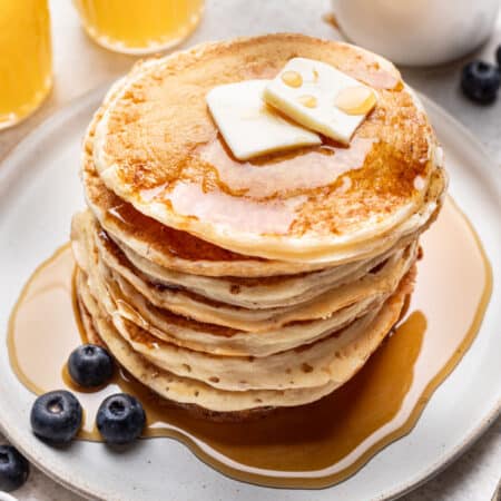 A stack of homemade buttermilk pancakes topped with pats of butter and syrup.