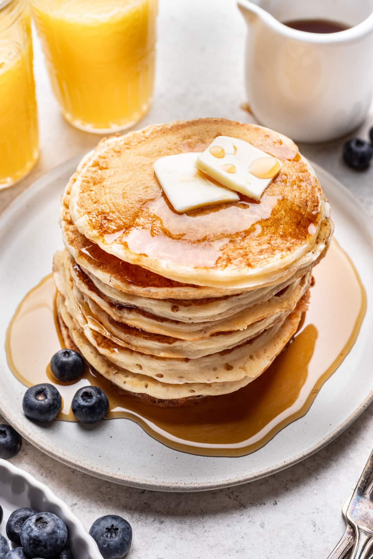 A stack of homemade buttermilk pancakes topped with pats of butter and syrup.