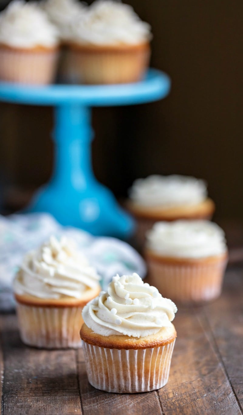 White cupcakes next to and on a blue cake stand