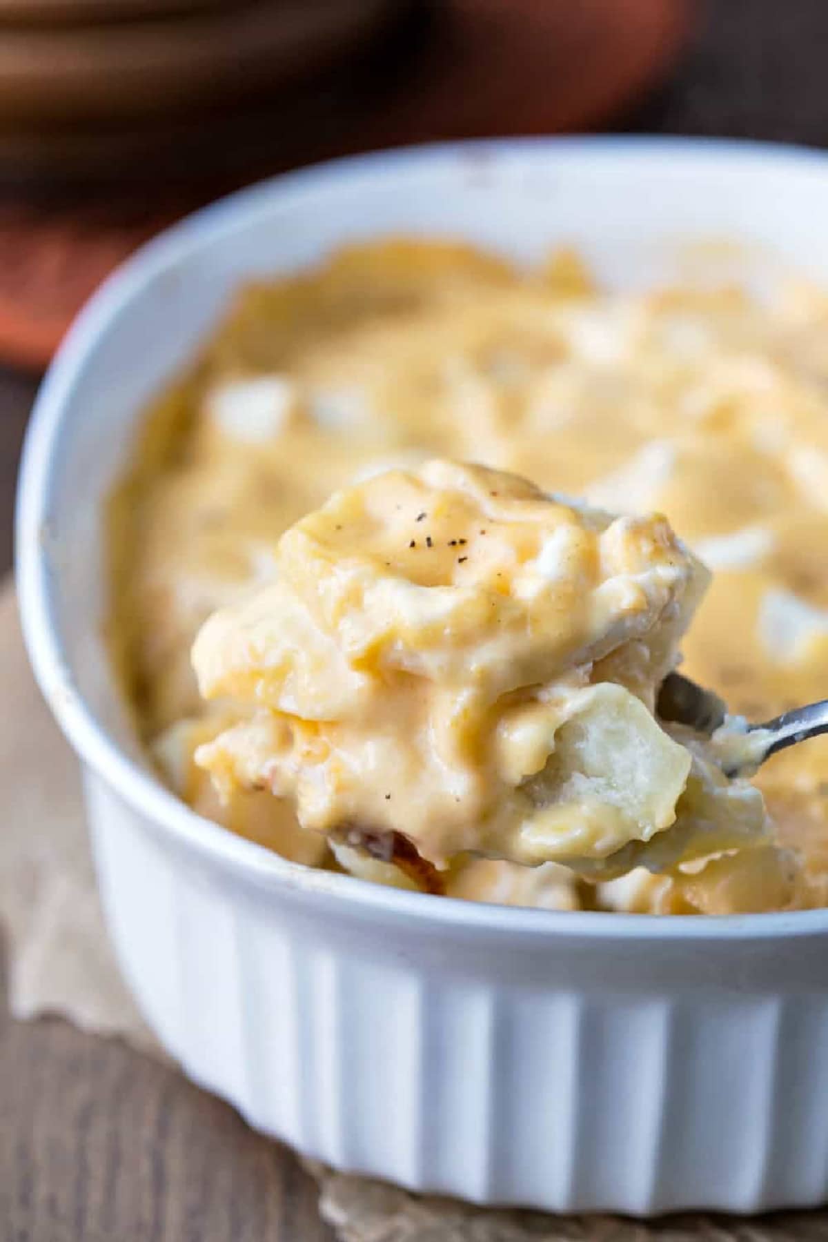 Silver spoon lifting a scoop of cream cheese scalloped potatoes.