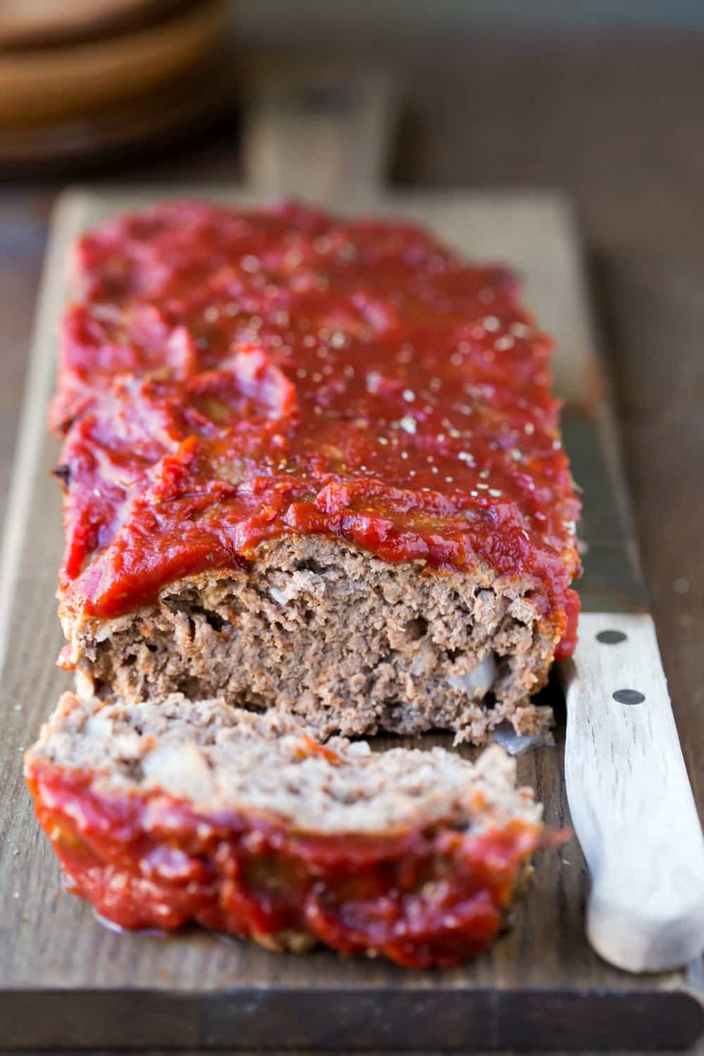 Meatloaf covered with chili sauce next to a wooden knife