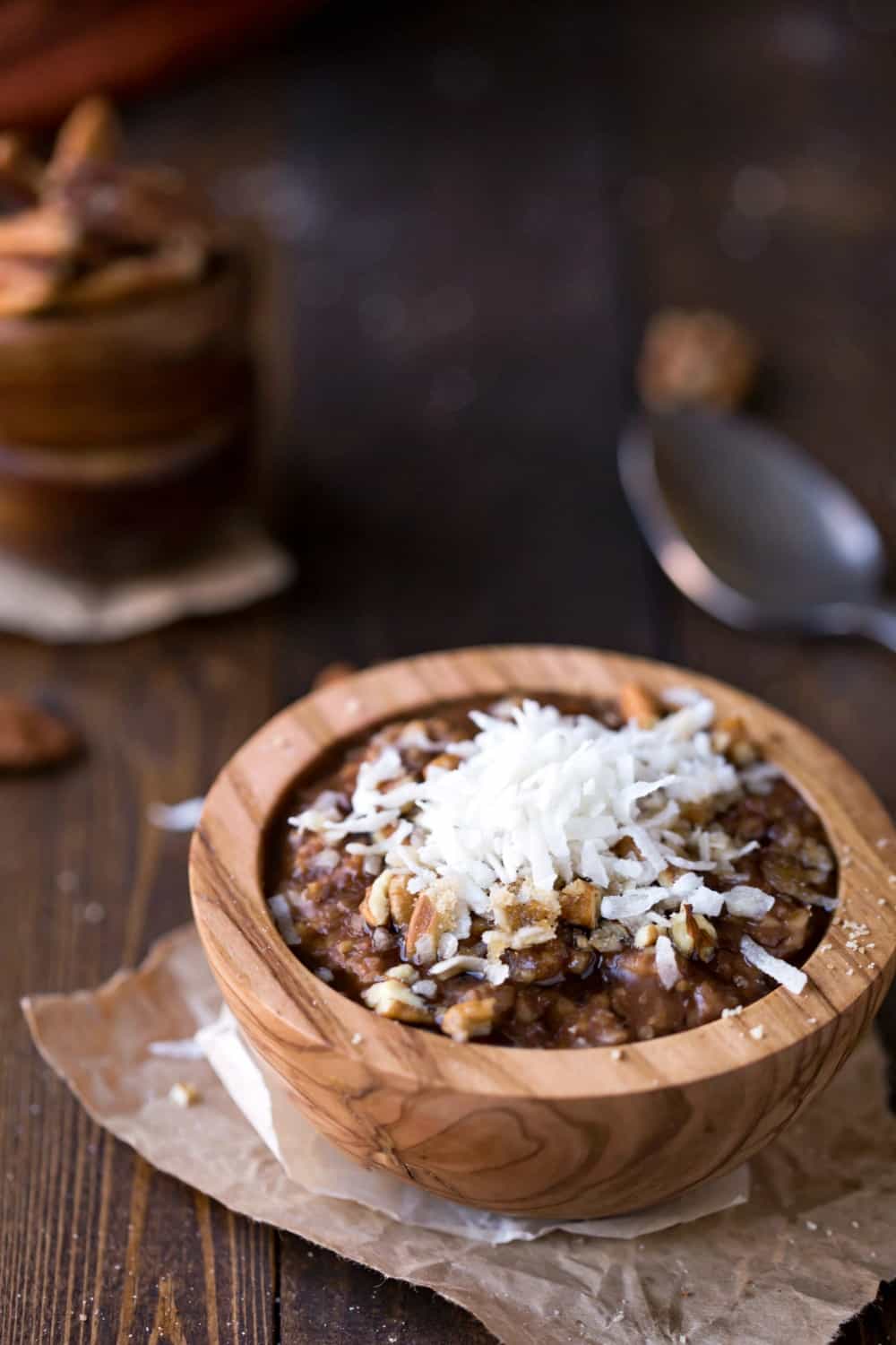 Crock Pot German Chocolate Oatmeal topped with coconut and pecans in a wooden bowl next to a spoon