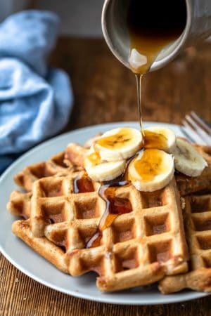 Maple syrup pouring onto slices of banana on banana bread waffles.