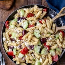 Dish of Greek pasta salad with wooden serving spoons in it