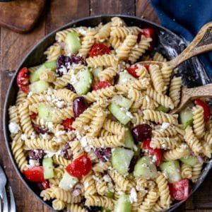 Dish of Greek pasta salad with wooden serving spoons in it