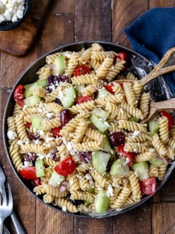 Dish of Greek pasta salad with wooden serving spoons in it