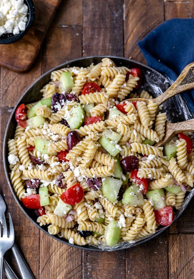 Dish of Greek pasta salad with wooden serving spoons in it