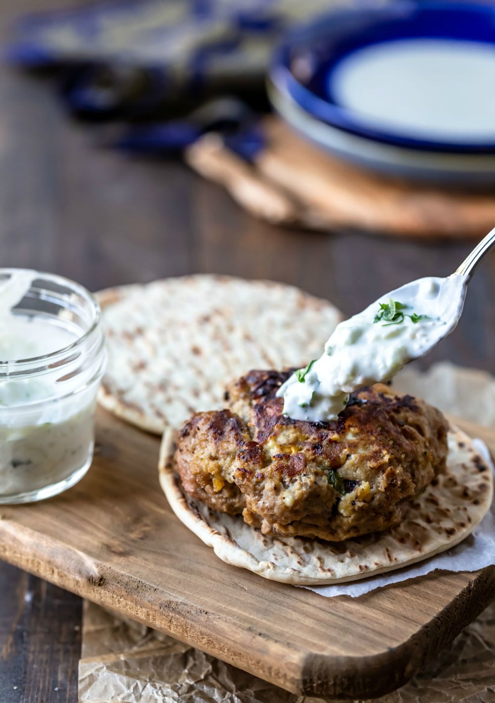 A spoon drizzling tzatziki on Greek chicken burger 