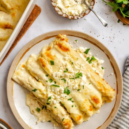 A plate of white chicken enchiladas topped with cilantro and queso fresco.