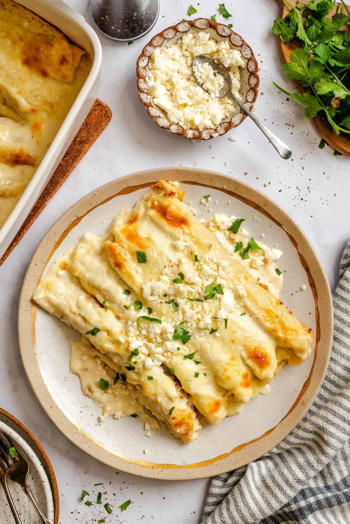 A plate of white chicken enchiladas topped with cilantro and queso fresco.