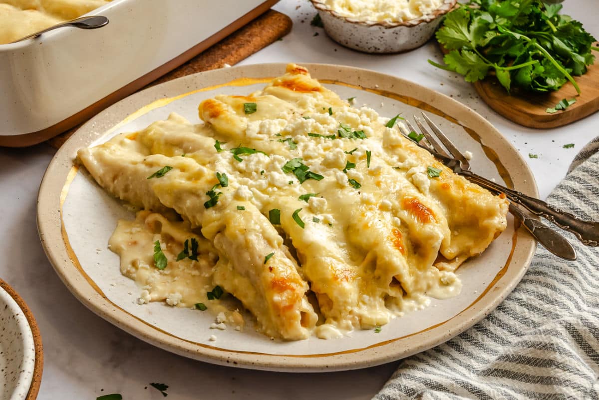 White chicken enchiladas on a plate next to a fork. 
