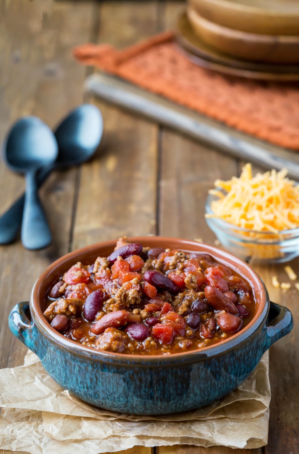 Barbecue Chili in a blue dish next to spoons and a dish of cheese