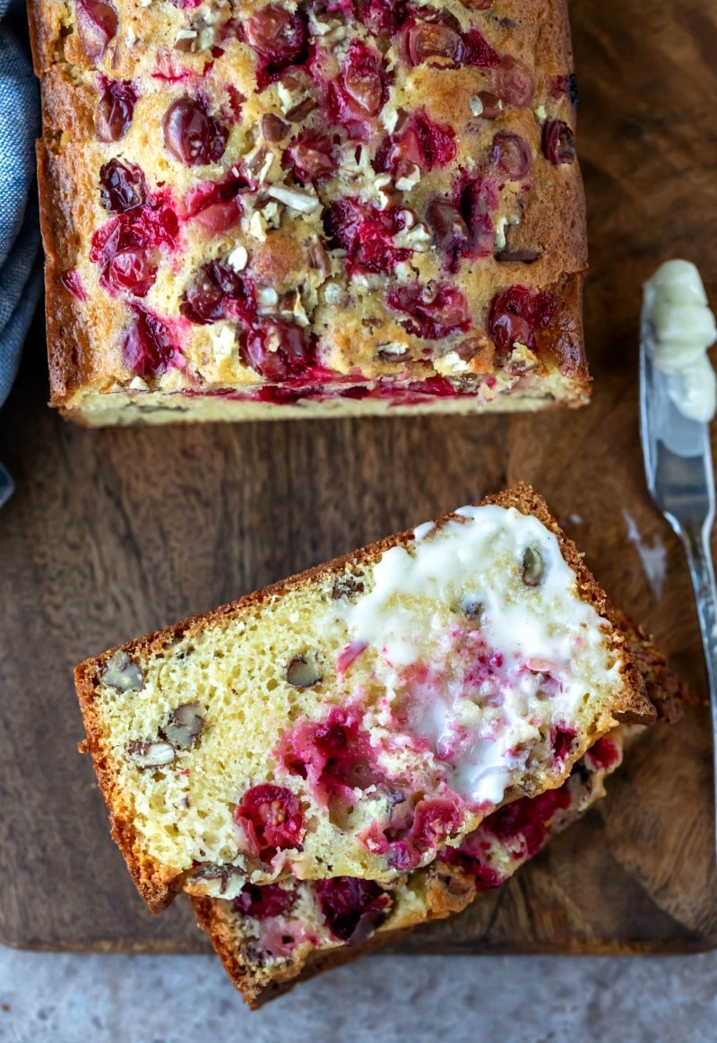 Partially buttered slice of cranberry nut bread on a wooden cutting board
