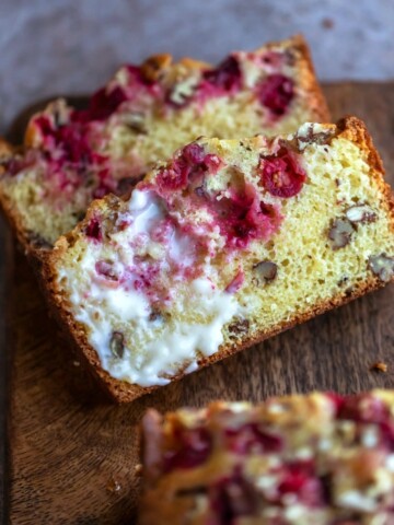 Two slices of cranberry nut bread on a wooden cutting board