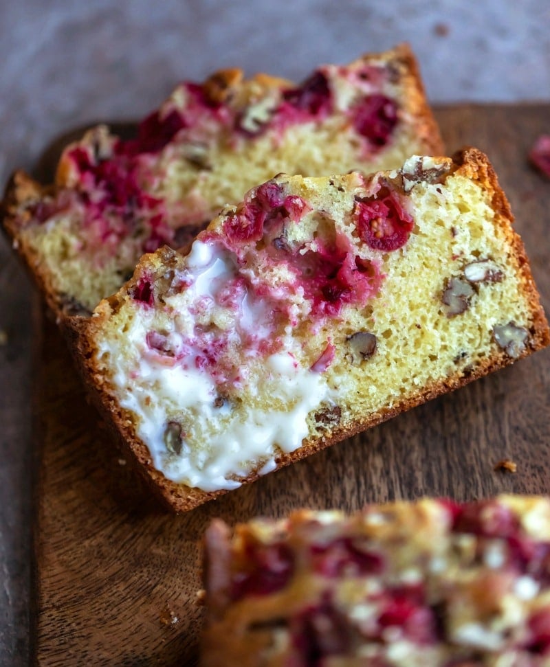 Two slices of cranberry nut bread on a wooden cutting board