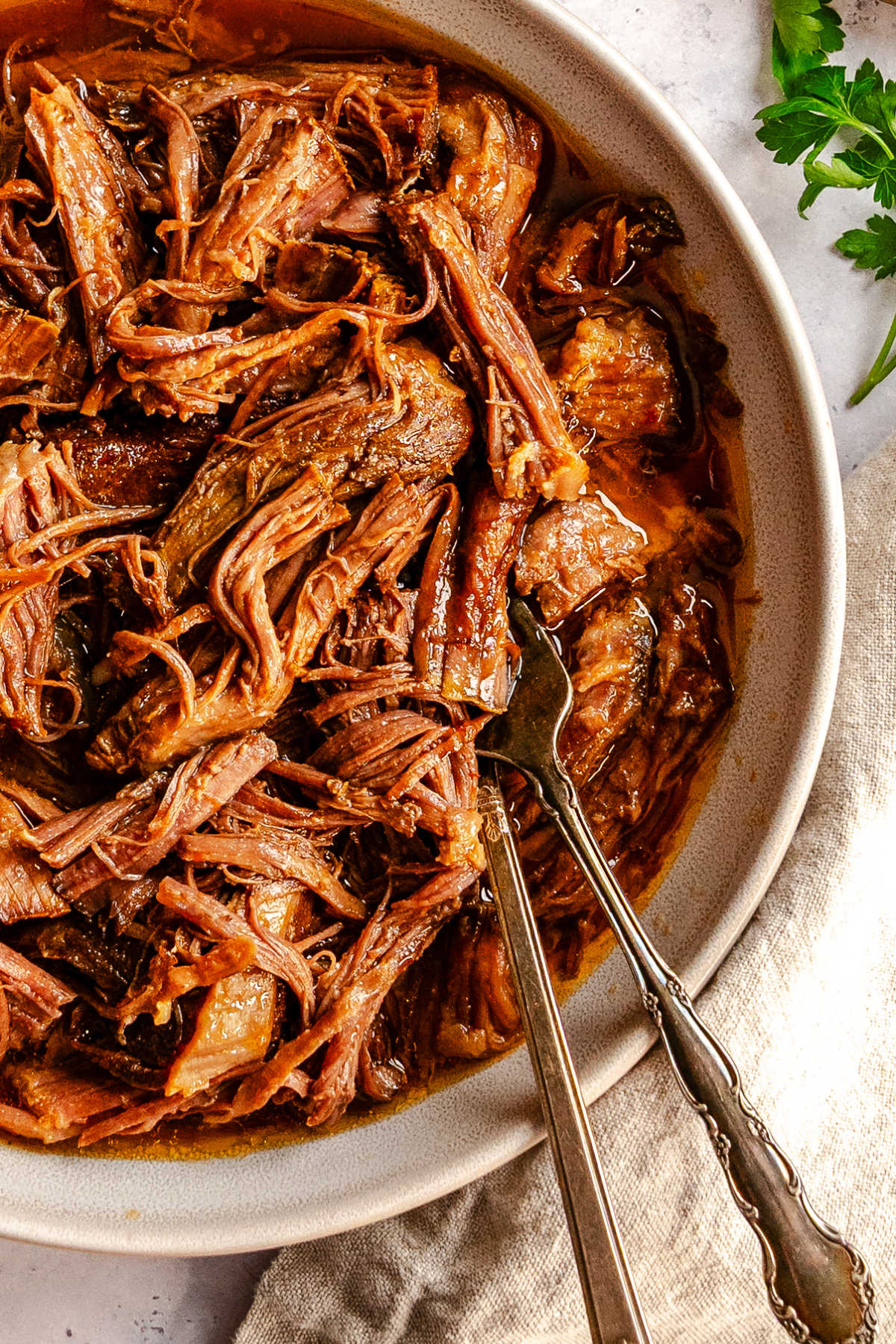 Close up of shredded pineapple chipotle beef in a dish with two forks.