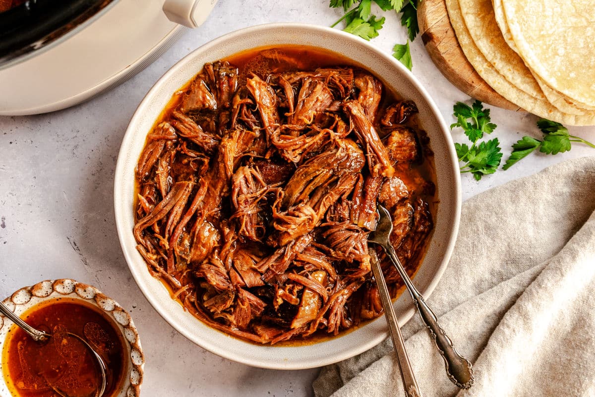 A dish of shredded chipotle pineapple beef next to a slow cooker.