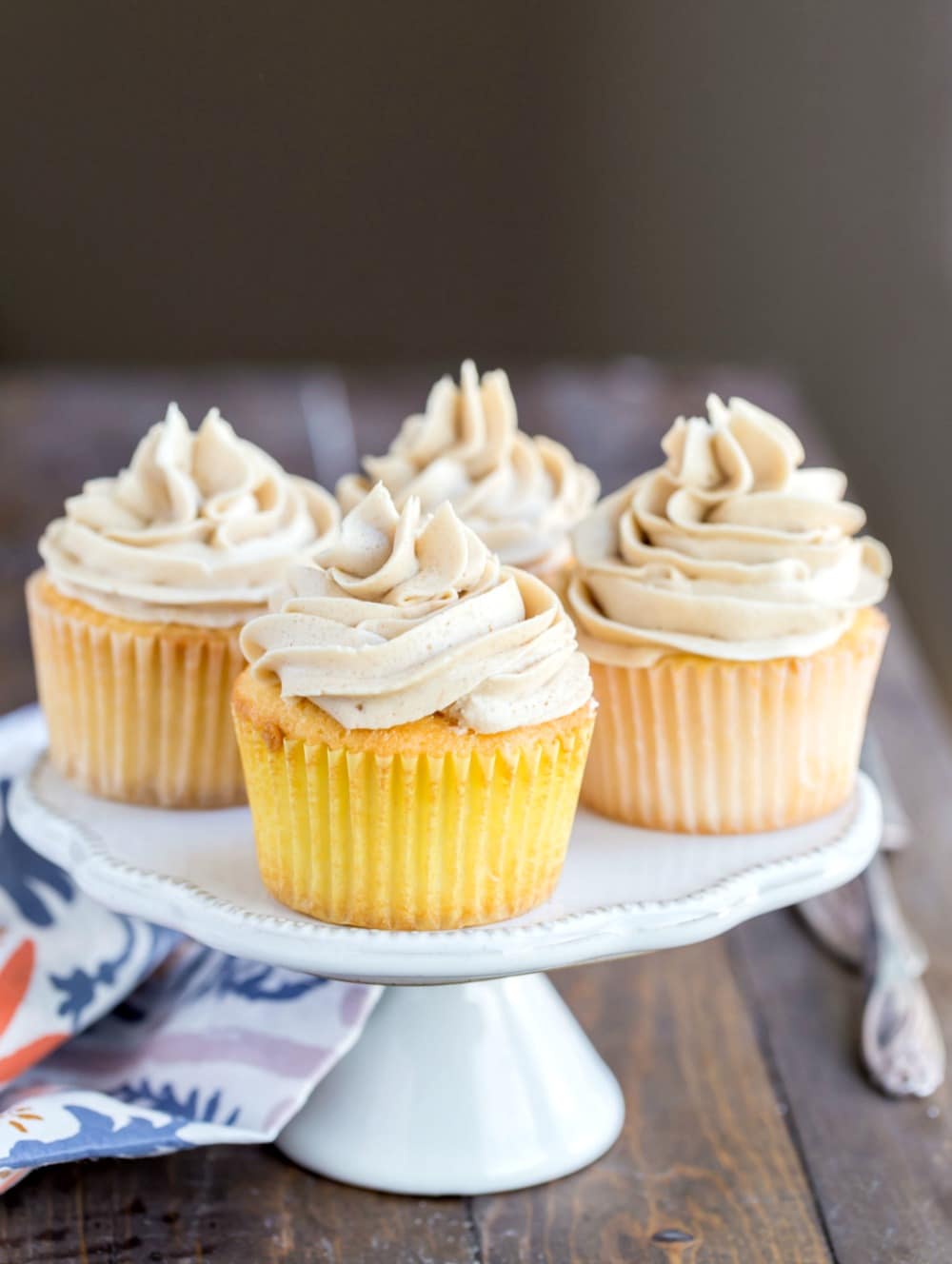 Whipped brown sugar buttercream frosting on vanilla cupcakes that are sitting on a white cake stand