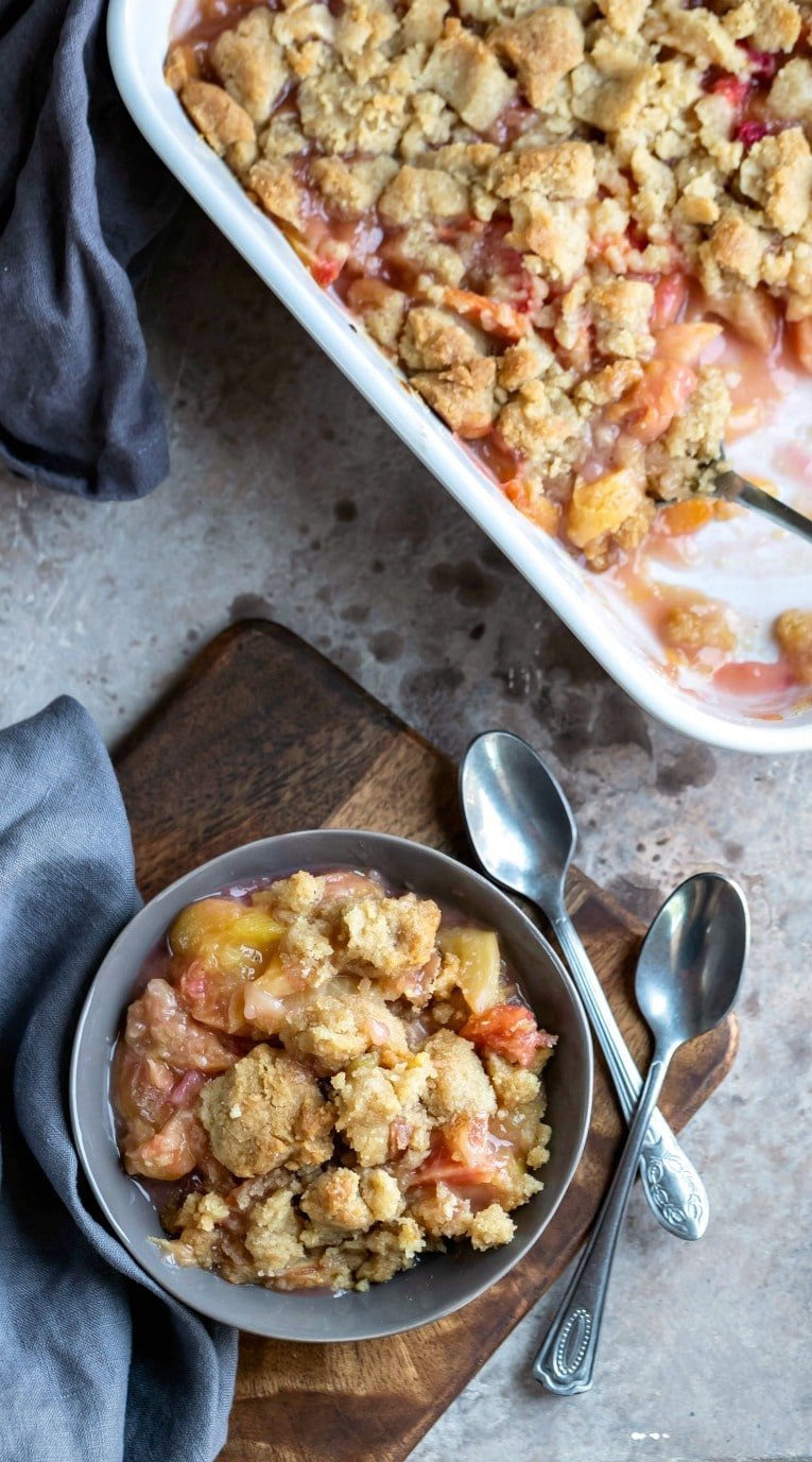 Gray dish with peach crumble next to two spoons