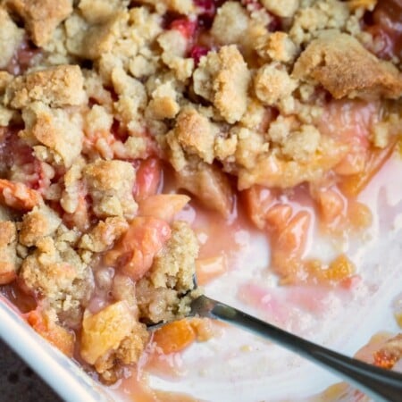 A white dish with peach crumble with a spoon in it.