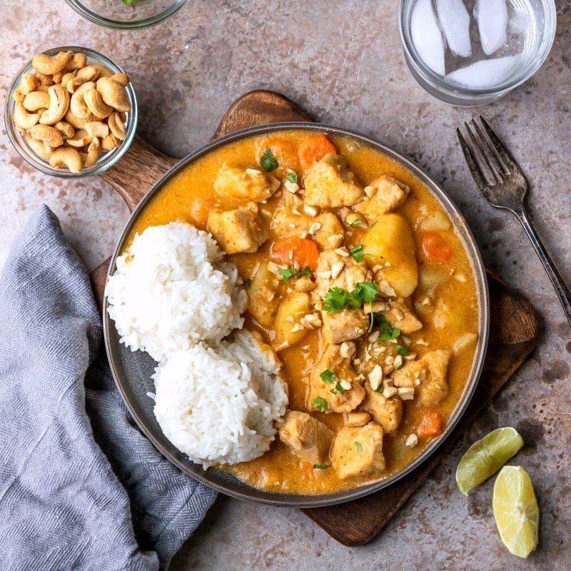 A plate of chicken Massaman Curry next to two lime slices