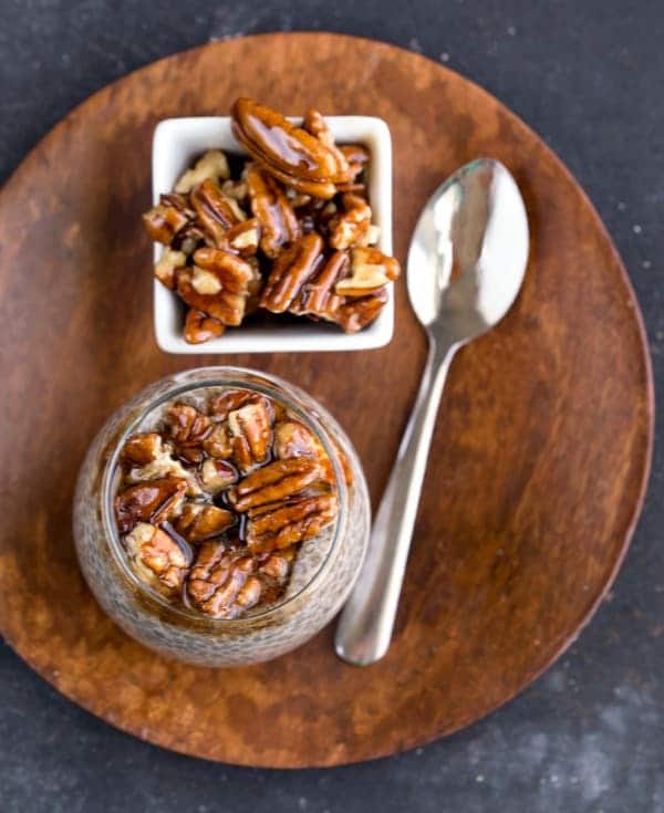 Sticky Bun Chia Seed Pudding in a glass jar next to a dish of sticky bun nut topping and a spoon