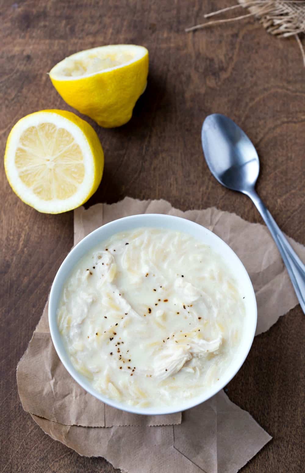 bowl of avgolemono soup next to a spoon and a sliced lemon