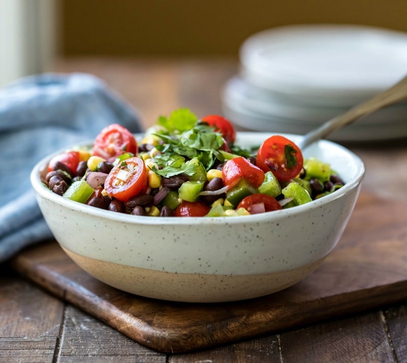 Bowl of black bean salad on a wooden cutting board