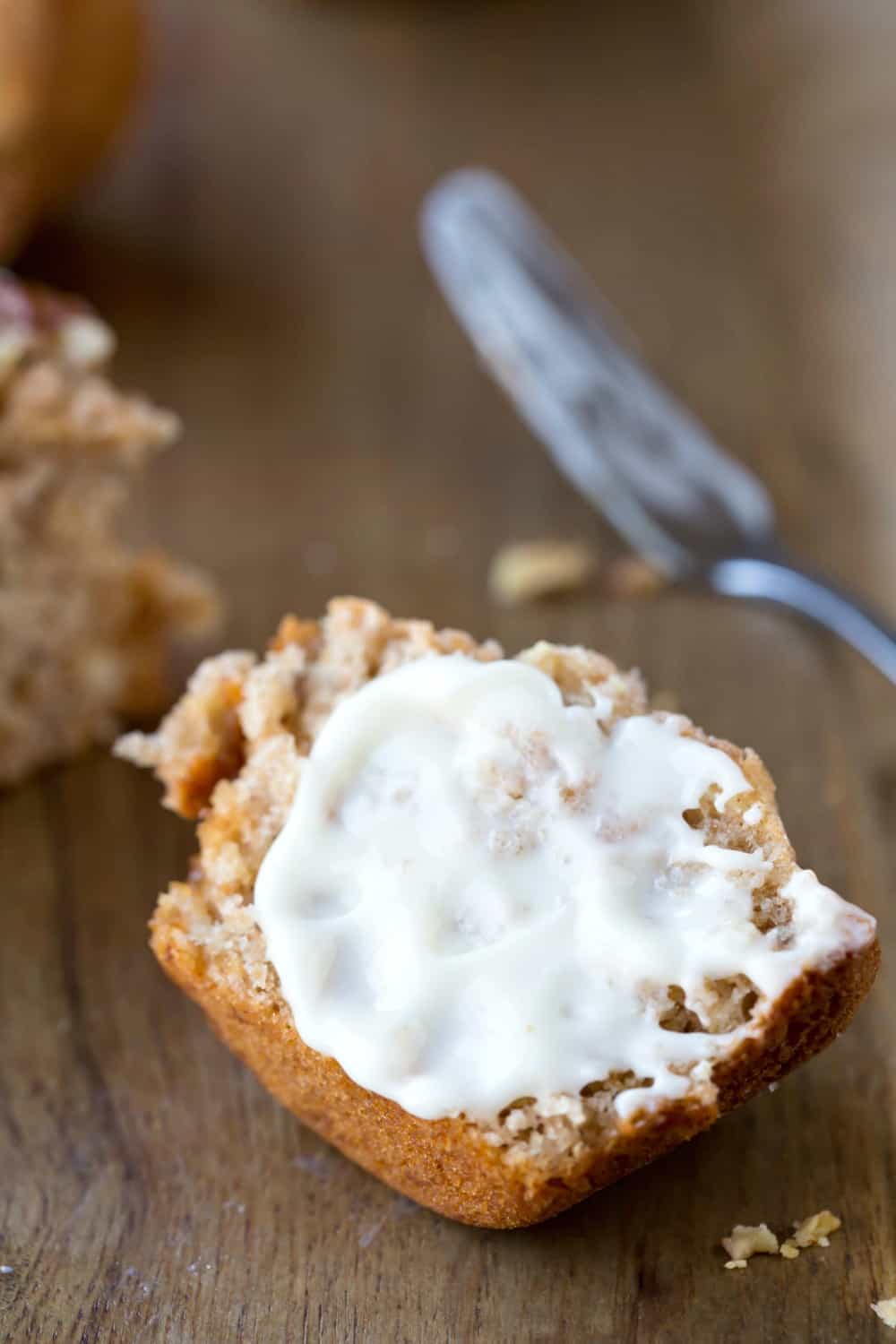 Half of a Cream Cheese Banana Muffin with butter on it next to a butter knife