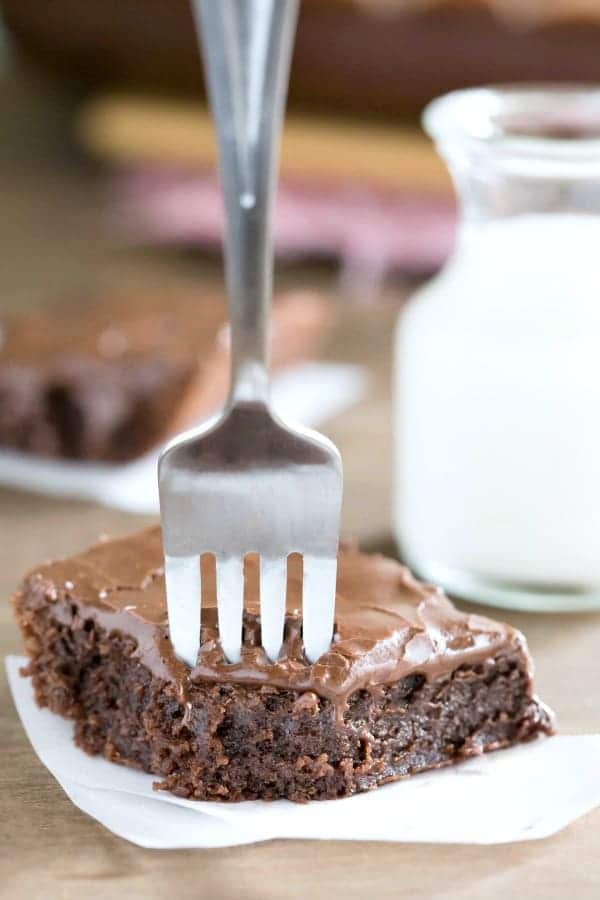 Frosted Brownie with a fork in it next to a glass of milk