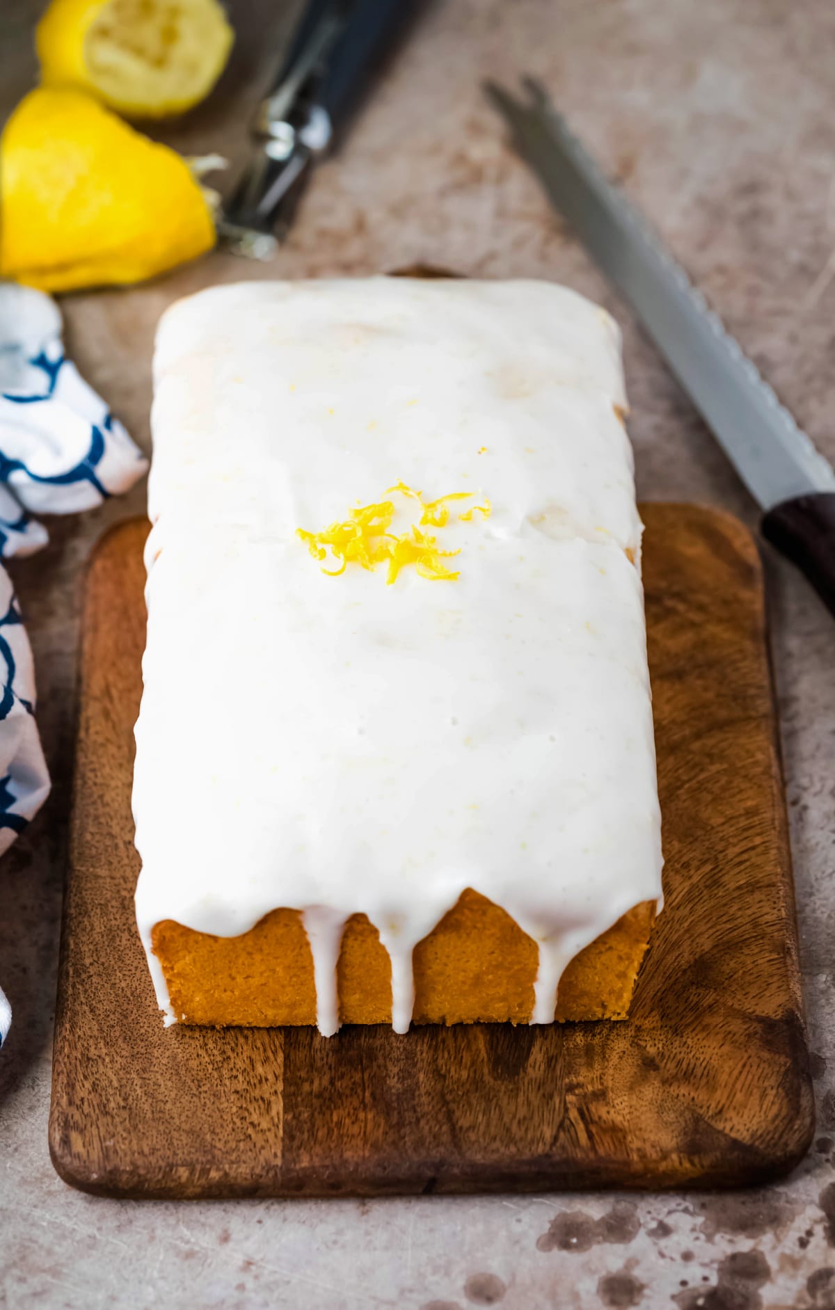 Iced lemon loaf cake on a wooden cutting board next to a bread knife