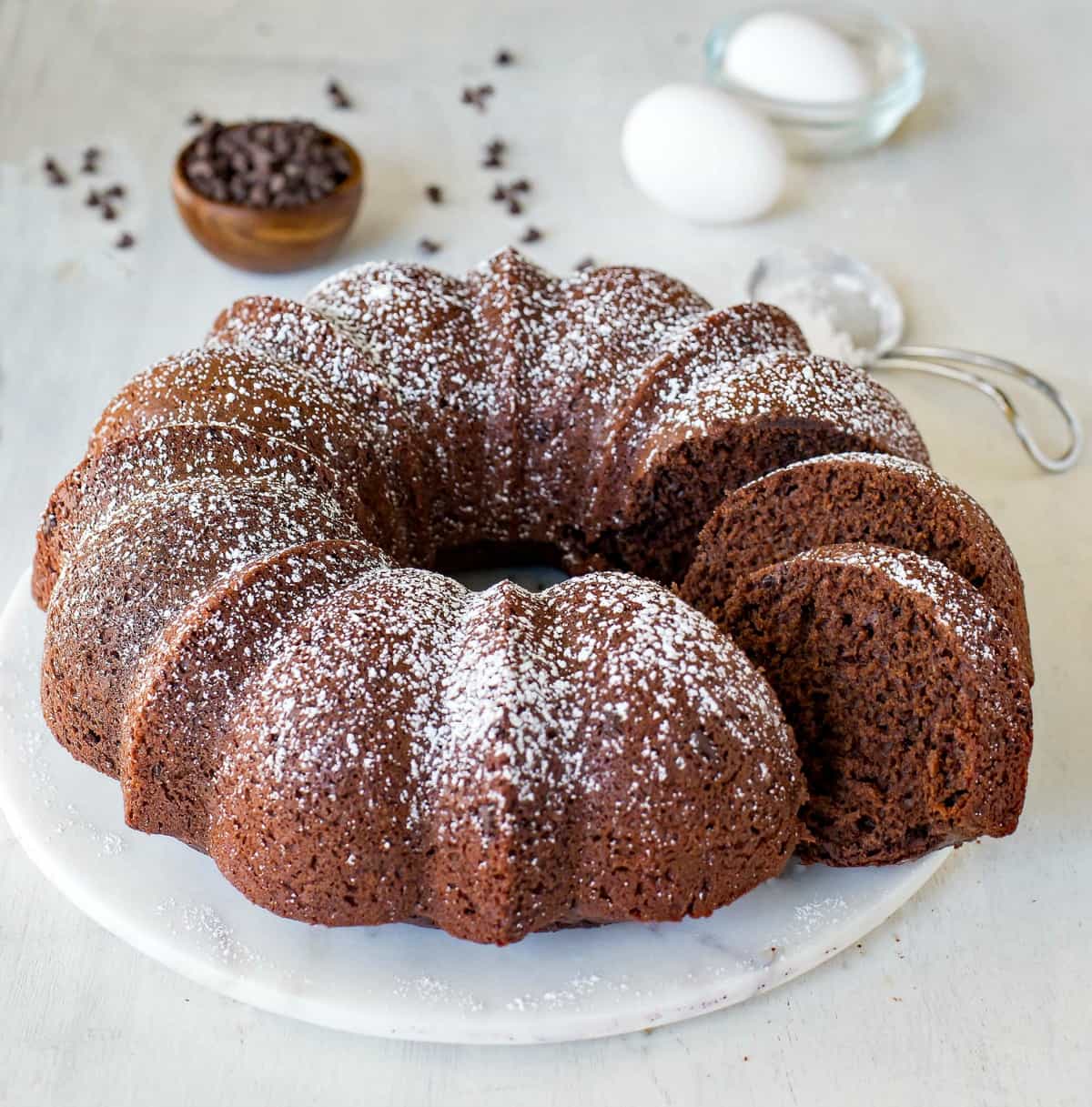 Chocolate bundt cake on a marble tray next to a bowl of chocolate chips