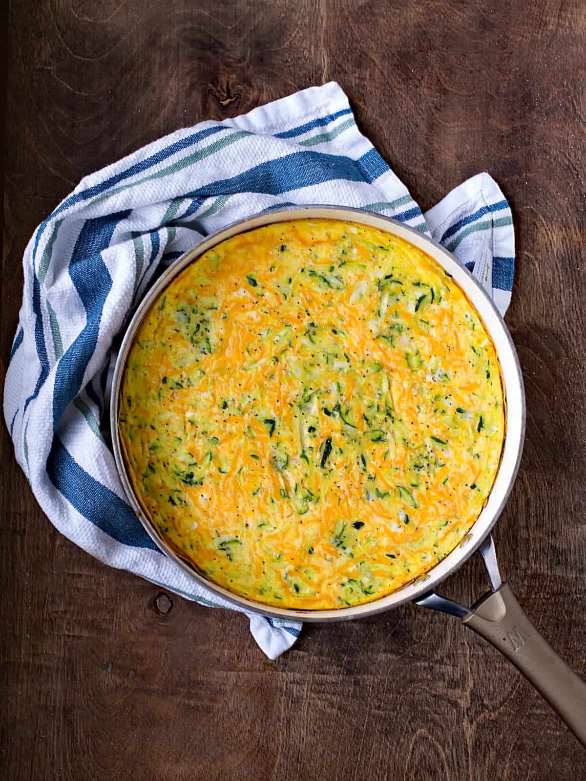 Zucchini Frittata in a skillet with a blue dish towel on a wooden board