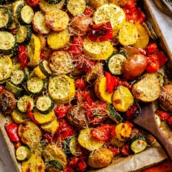 A wooden spoon holding a scoop of roasted summer vegetables on a baking tray.