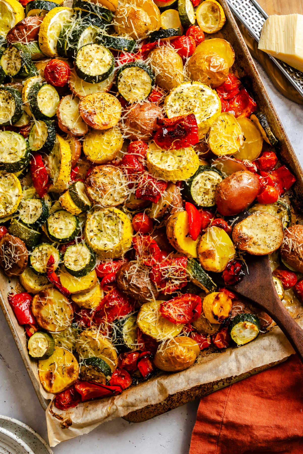 A wooden spoon holding a scoop of roasted summer vegetables on a baking tray.