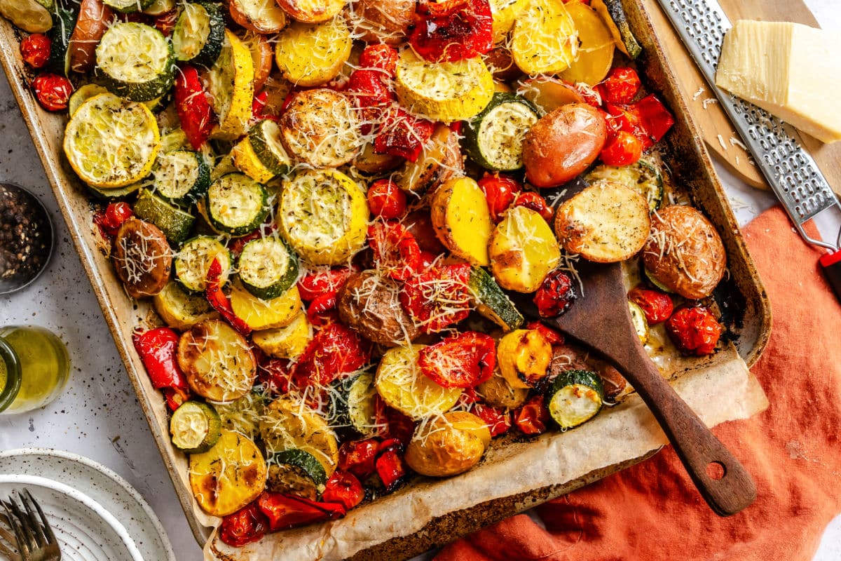 A sheet pan of roasted summer vegetables next to an orange kitchen linen. 