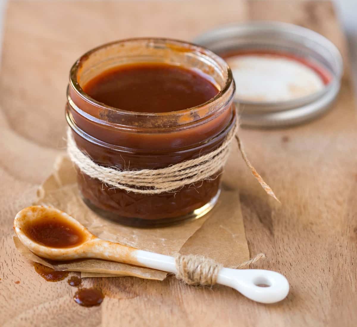 Dr Pepper Barbecue Sauce in a glass jar next to a white spoon. 