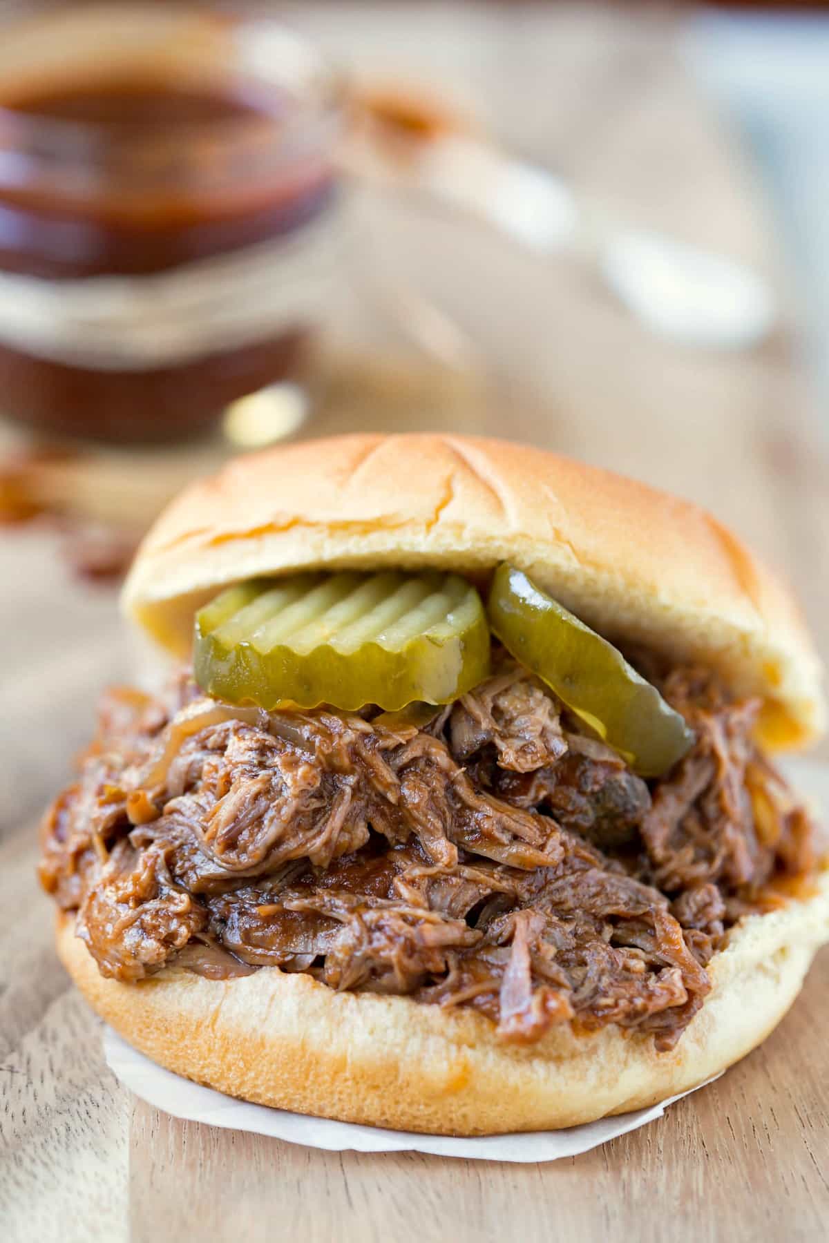 Slow Cooker Barbecue Beef sandwich on a piece of parchment paper on a wooden cutting board